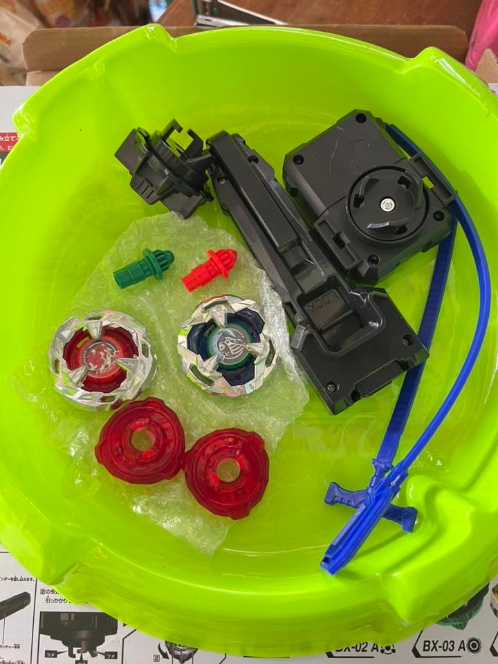 Toy parts including spinning tops and a black mechanism on a green tray.