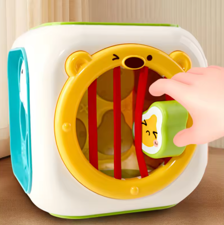 Toy with a bear design and a hand interacting with it on a wooden surface.
